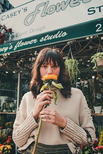 Person Standing In Front Of A Plant Store Holding A Stem Of Sunflower