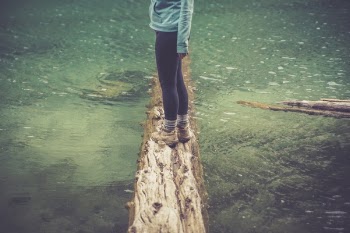Person Standing on a Brown Wood Log Floating on a Body of Water