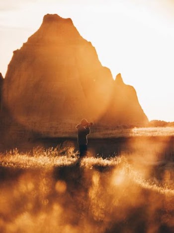 person standing on brown field taking photo of mountain