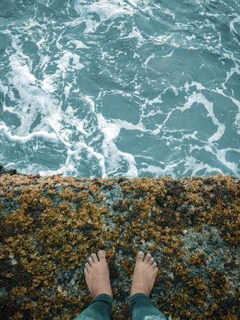Person Standing on Cliff Overlooking Body of Water