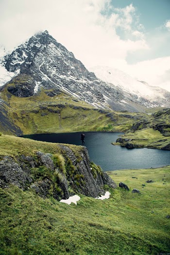 Person Standing on Edge of Cliff Overlooking Lake Below