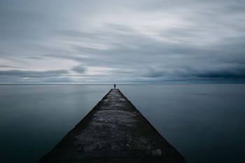 person standing on grey concrete pier under cloudy sky