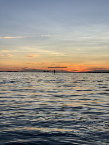 Person Standing on Paddle Board Under Orange Skies