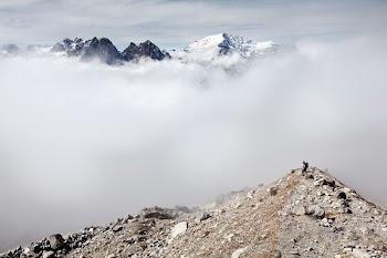 person standing on peak front of white clouds and ice-capped mountain