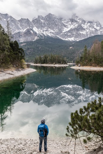 Person Standing on Riverbank Under Cloudy Day Sky