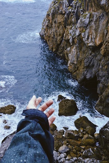 Person Standing On Rock Cliff Facing The Sea