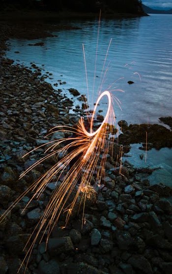 person standing on rock formation near body of water on steel wool photography
