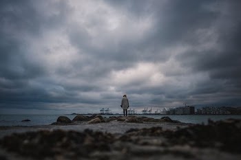 person standing on sea shore under dark clouds