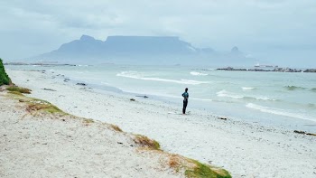 person standing on shore near mountain covering of fogs at daytime