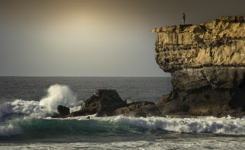 Person Standing on Top of Rock Formation Surrounded by Sea