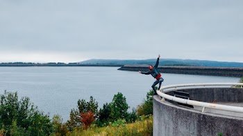 Person Standing on White Metal Rail With Both Hands Up Overlooking Body of Water