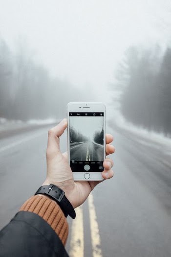 person taking photo of foggy asphalt road using silver iPhone 6