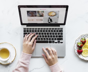 Person Using Black and Gray Laptop Beside White Ceramic Cup and Saucer on White Table