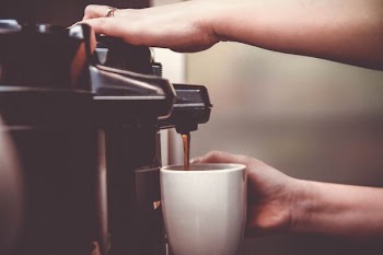 person using coffeemaker with white ceramic mug