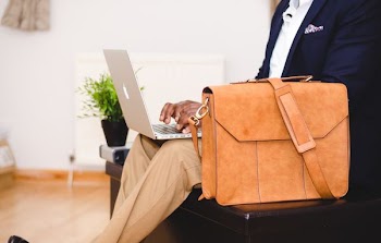 person using MacBook Pro beside brown leather briefcase
