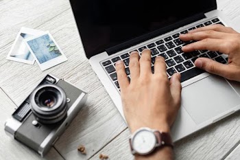 person using MacBook Pro beside film camera