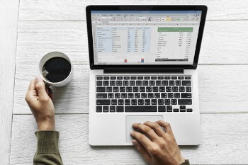 Person Using Macbook Pro While Holding White Ceramic Mug Filled With Black Coffee