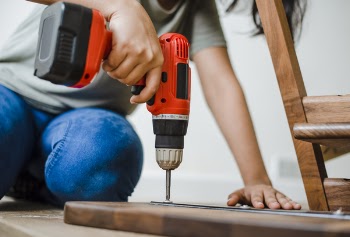 Person Using Red and Black Cordless Power Drill on Brown Wooden Bar