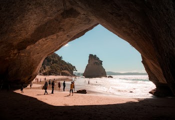 Person Walking Beside Cave and Body of Water