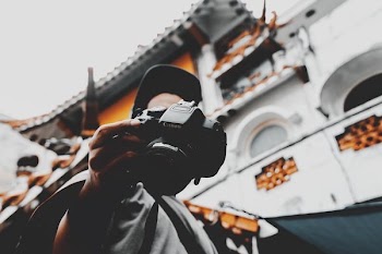 person walking near white building holding black Canon DSLR camera