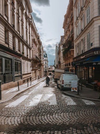 Person Walking On A Narrow Cobblestone Street With Parked Vehicles On The Side 