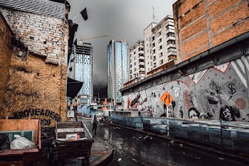 Person Walking On A Wet Street Along A Building With Mural Under Gray Sky