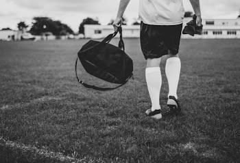 Person Walking on Field Holding Duffel Bag in Grayscale Photography