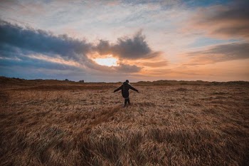 person walking on field under gray clouds