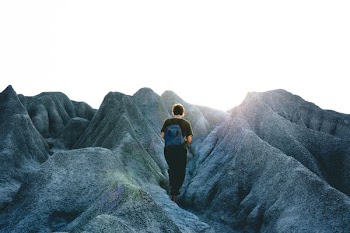 person walking on mountain under cloudy sky