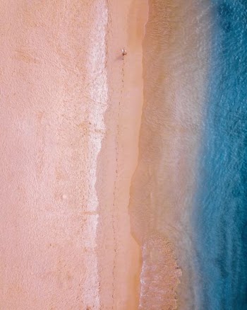 person walking on sand near seashore leaving foot trails