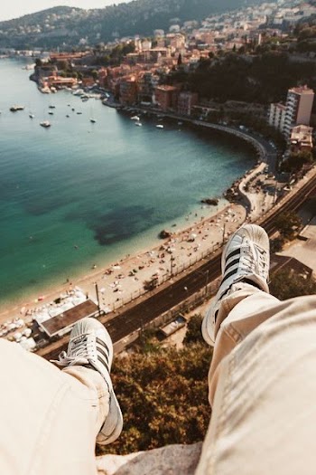 person wearing a pair of white adidas superstar sitting on a gray buildingf