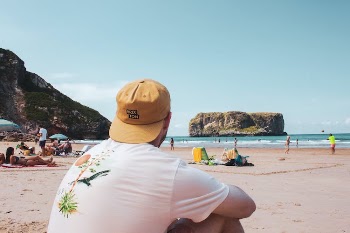 Person Wearing a Yellow Cap and White Shirt Sitting on Sand