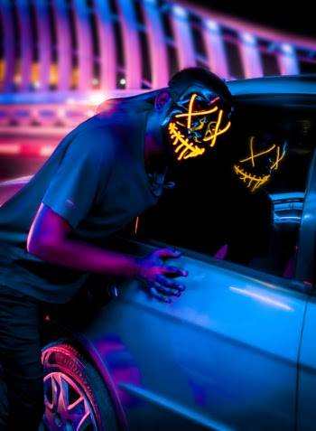 Person Wearing Black and Yellow X Face Mask Beside Silver Car