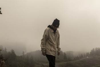 Person Wearing Black Beanie and Beige Jacket Walking on Grass Field