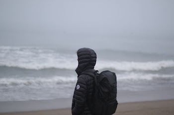 person wearing black duffle coat facing body of water