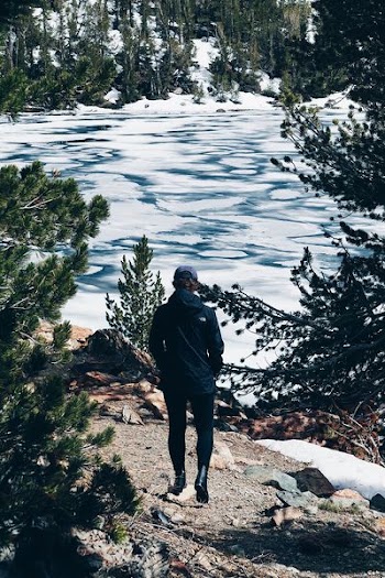 person wearing black jacket and blue hat walking on brown soi;l
