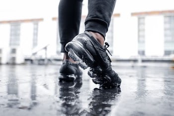 person wearing black Nike Vapormax shoes on wet floor