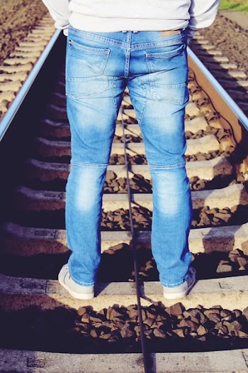 Person Wearing Blue Denim Pants While Standing on Brown Train Rail