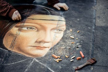 person wearing brown long-sleeved shirt painting portrait of woman on black concrete pavement