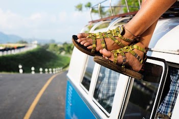 person wearing brown strappy flat sandals sitting on van