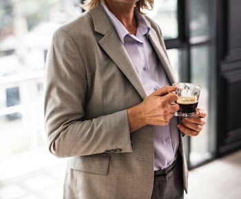 person wearing brown suit jacket holding cup of coffee