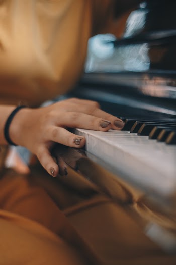 Person Wearing Brown Top Holding on Piano Keys