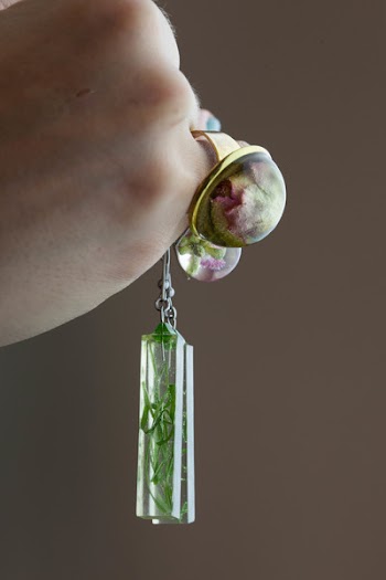 Person Wearing Gold-colored Flower Bubble Ring While Holding Rectangular Green Leaf Paperweight Pendant