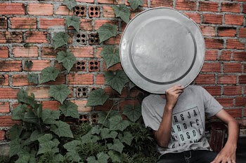 Person Wearing Gray Crew-neck T-shirt holding a tray on the face next to a brick wall 