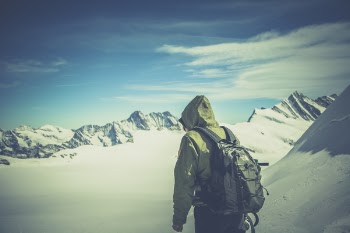 Person Wearing Green Jacket Walking on White Snow Covered Mountain
