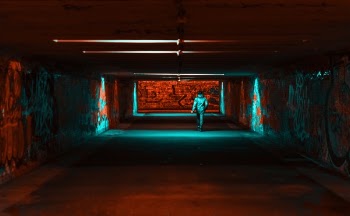 Person Wearing Jacket Walking on Tunnel With Red and Green Lights