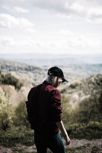 Person Wearing Maroon Jacket and Blue Jeans Standing on Mountain Scenery