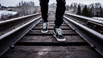 person wearing pair of black-and-white Vans Old Skool shoes walking on brown train tracks during winter