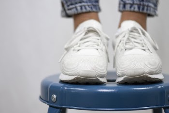 Person Wearing Pair of White Sneakers Stepping on Stool