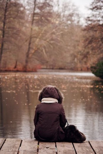 person wearing parka jacket sitting on wooden dock